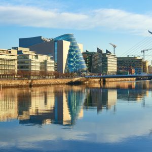 Modern buildings and offices on Liffey river in Dublin on a bright sunny day. Bridge on the right is a famous Harp bridge.